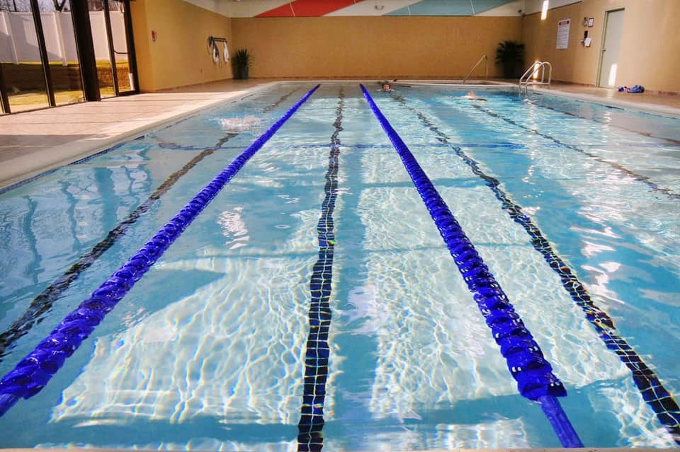Indoor lap pool with blue lane dividers under yellow-painted ceiling with skylight