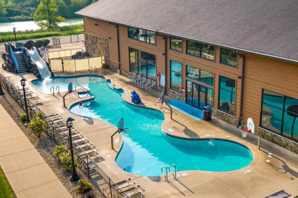Resort pool complex with water slide, kiddie pool, indoor/outdoor facilities, and lakeside setting