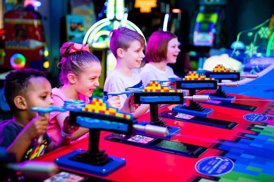 Children playing arcade games with neon lights and colorful game machines indoors