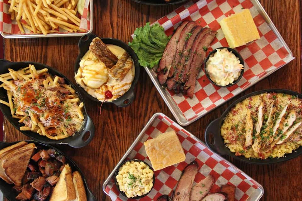 Overhead view of gourmet barbecue spread with meats, sides, fries, and checkered serving trays