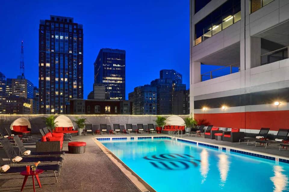 Rooftop pool with red loungers overlooking city skyline at night