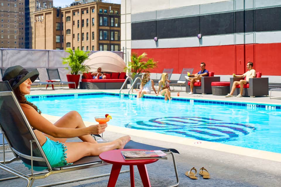 Urban rooftop pool with lounge seating, red accent wall, and city buildings