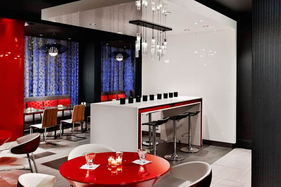 Modern bar lounge with red accents, white counter, blue curtains, pendant lighting, and lounge seating