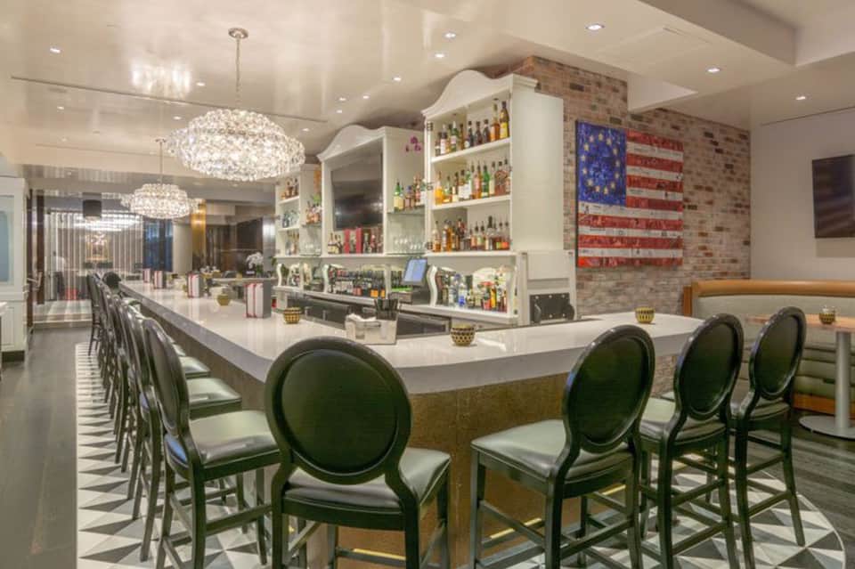 Modern resort bar with elegant crystal chandeliers, brick wall, and stocked shelves