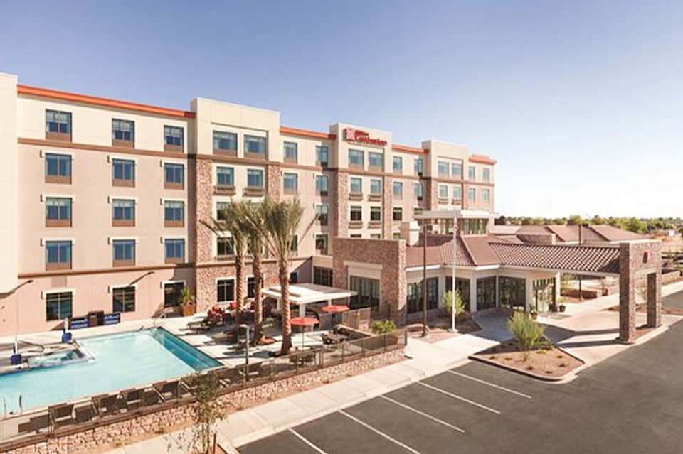 Contemporary hotel exterior with pink and coral facade, pool area, and palm trees