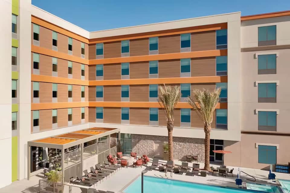 Modern hotel courtyard with colorful building facades, palm trees, and ground-floor pool area
