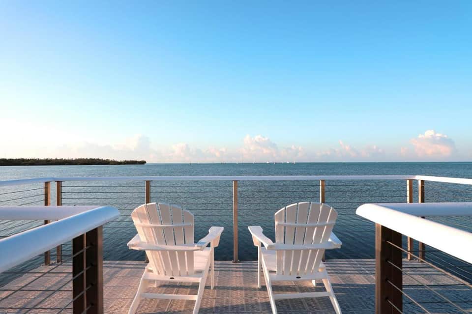 White Adirondack chairs on waterfront deck overlooking calm bay with tree-lined horizon