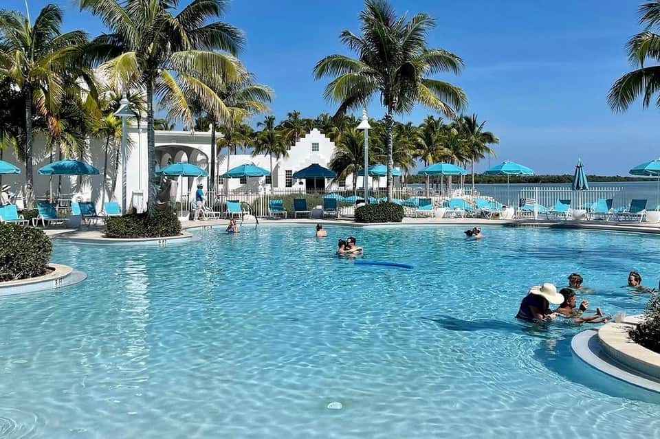 Lagoon-style resort pool with white structures, palm trees, and families swimming