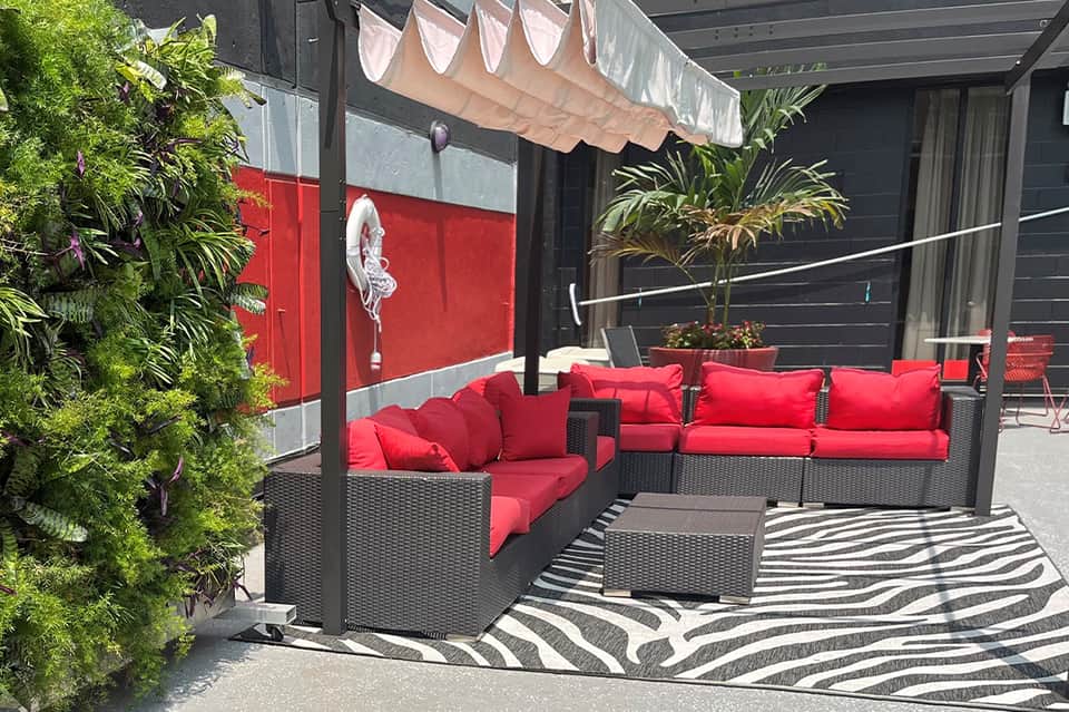 Modern patio lounge with red cushioned seating, black pergola, green living wall, and striped area rug
