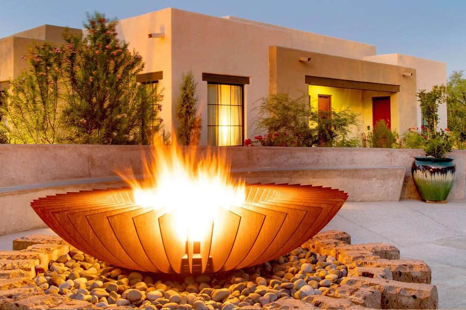Modern desert villa courtyard with fire pit, contemporary architecture, and illuminated windows at dusk