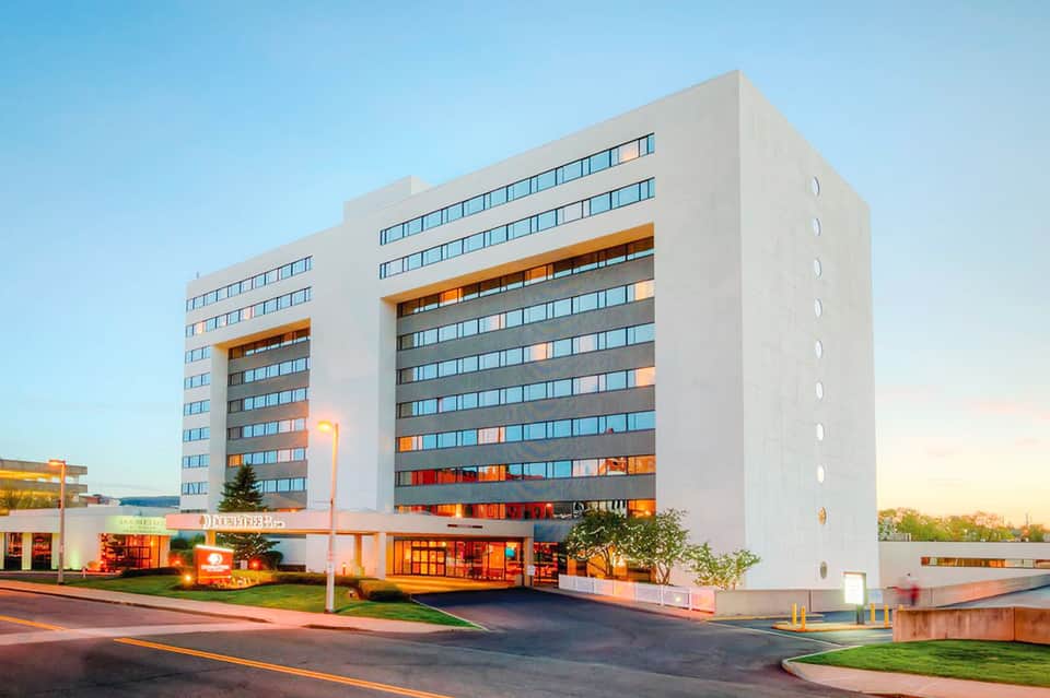 Modern multi-story hotel building with white facade and orange accents, illuminated at dusk