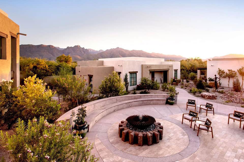 Desert resort courtyard with circular fire pit, lounge chairs, and mountain sunset views