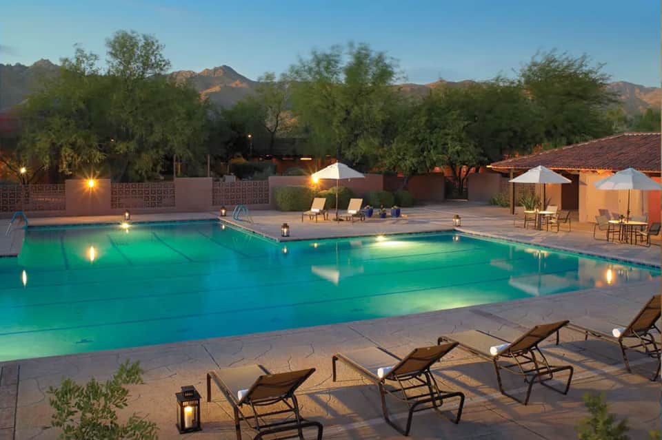 Illuminated resort pool at dusk with lounge chairs and mountain backdrop