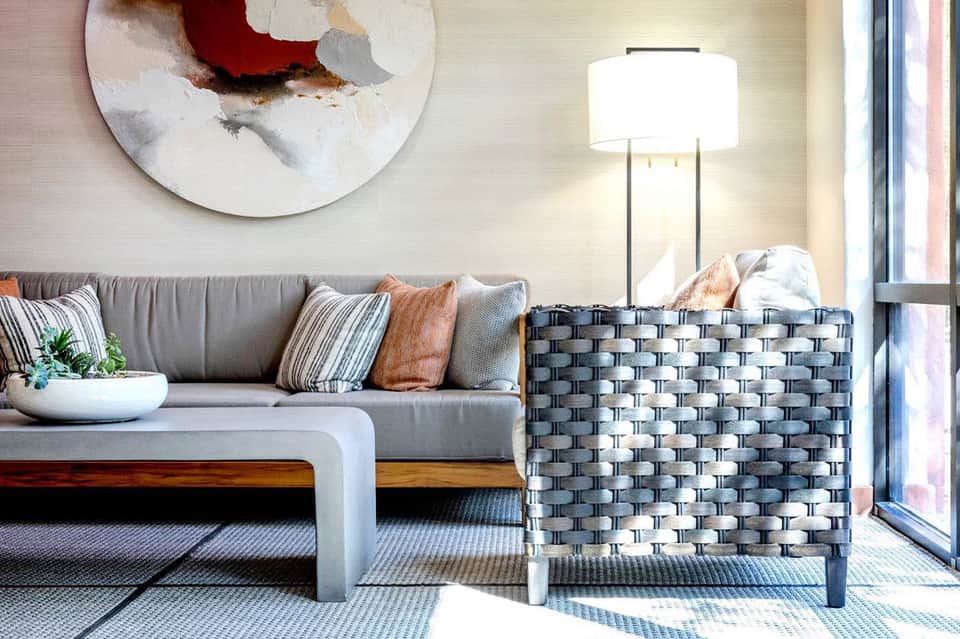Contemporary living room with gray sofa, woven accent chair, abstract artwork, and floor lamp