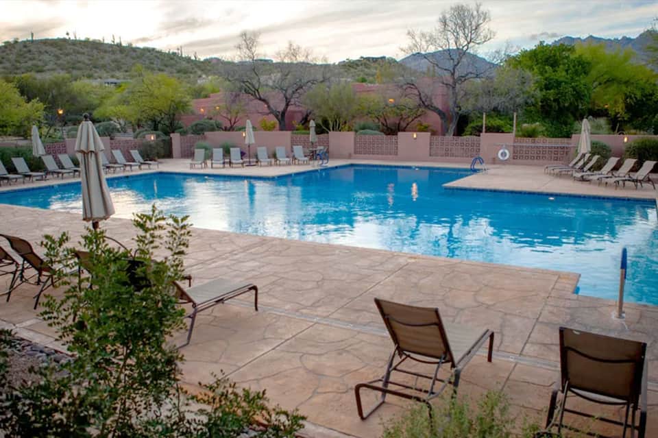 Expansive resort pool with desert mountain backdrop, lounge chairs, umbrellas, and surrounding landscaping