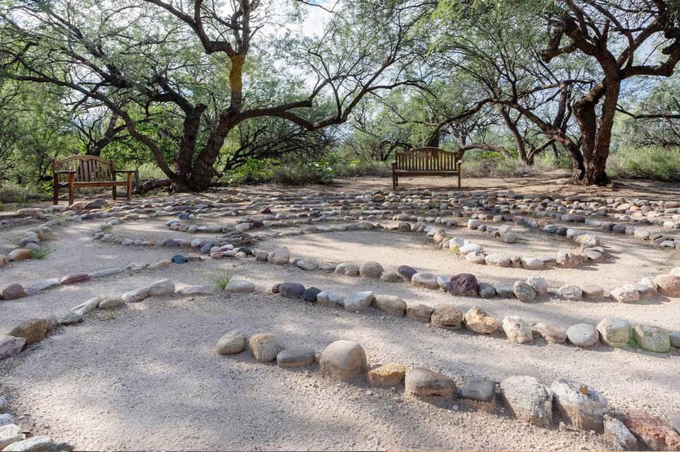 Labyrinth path made of stones under large shade trees with benches
