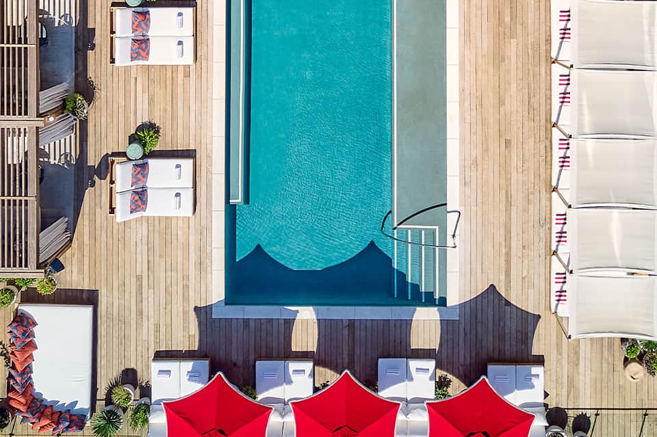 Overhead view of resort pool with red umbrellas, wooden decking, and lounging areas