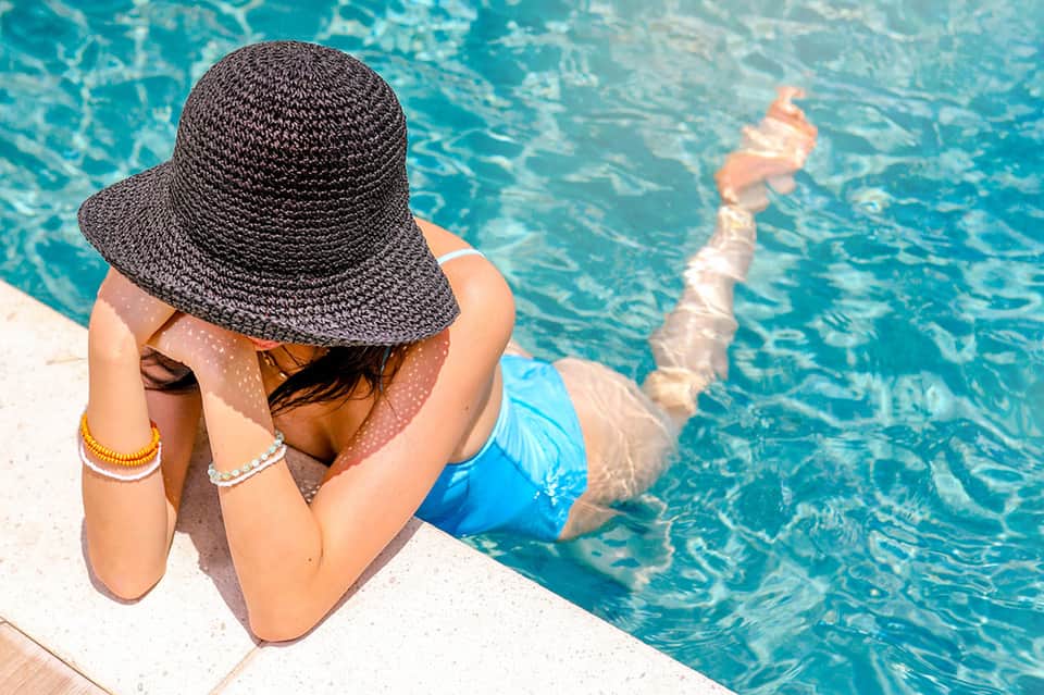 Woman in black hat sitting poolside overlooking turquoise water