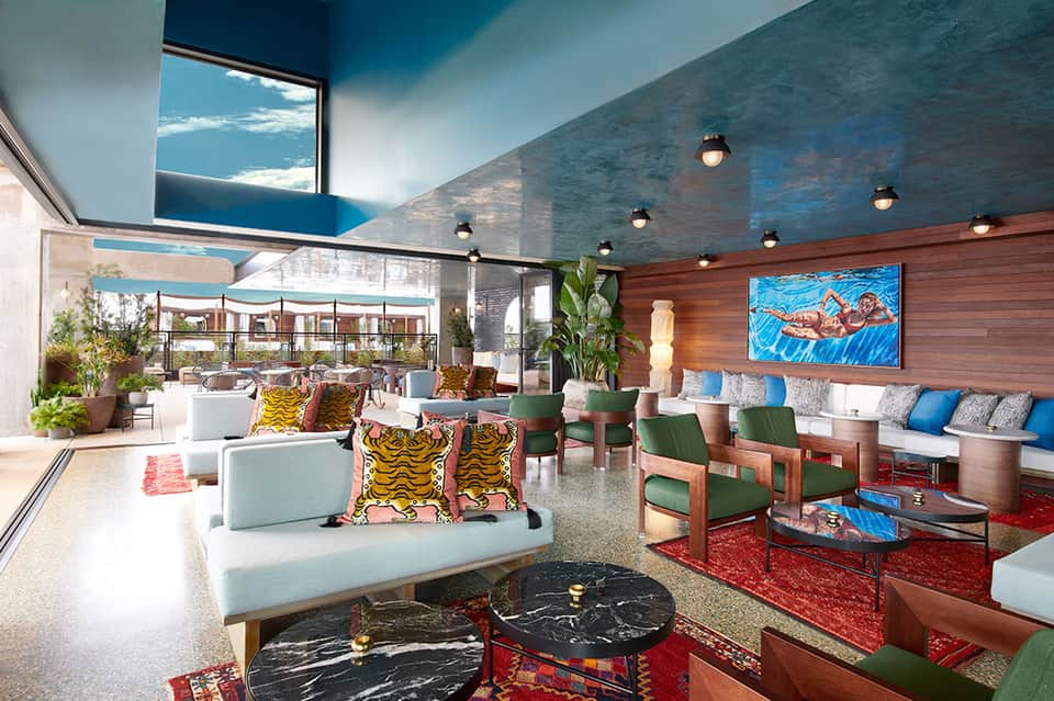 Modern lounge with blue ceiling, colorful pillows, wood accents, and outdoor terrace view