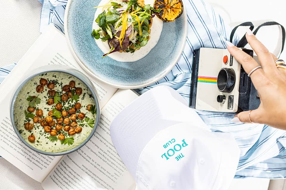 Fine dining dishes with soup and salad, magazine, and instant camera on blue striped cloth