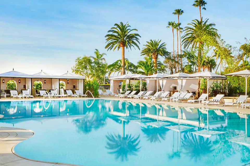 Turquoise resort pool with palm trees, white cabanas, and lounge chairs under blue sky