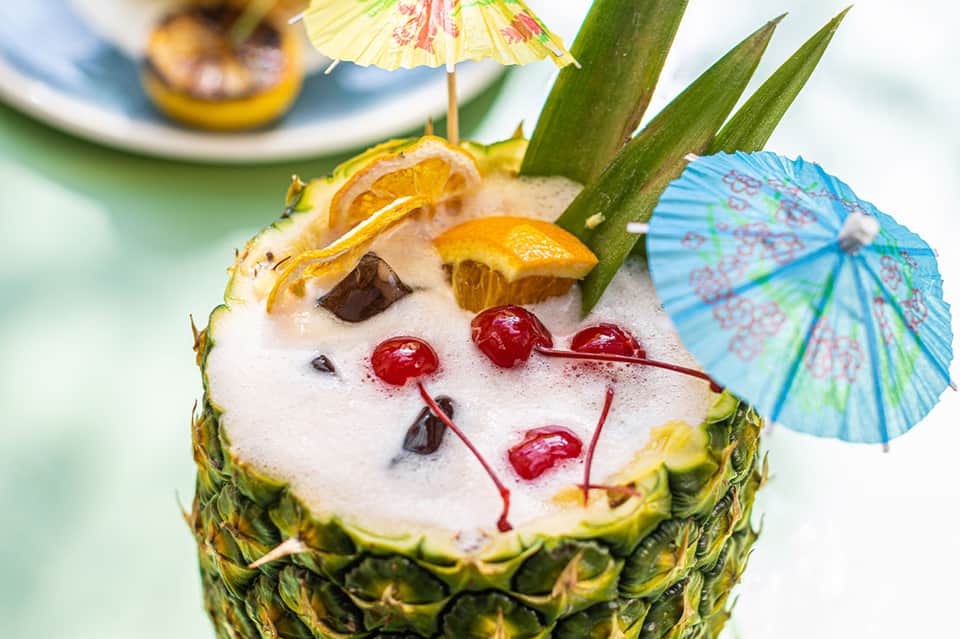 Tropical cocktail served in pineapple with decorative umbrella and fresh fruit garnish