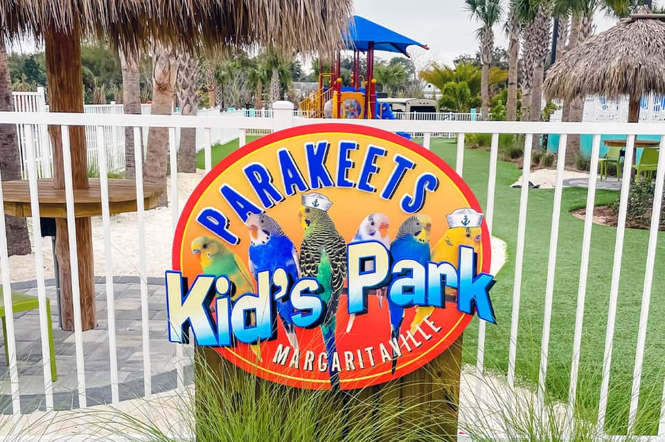 Colorful kids park sign with playground equipment, palm trees, and white picket fence