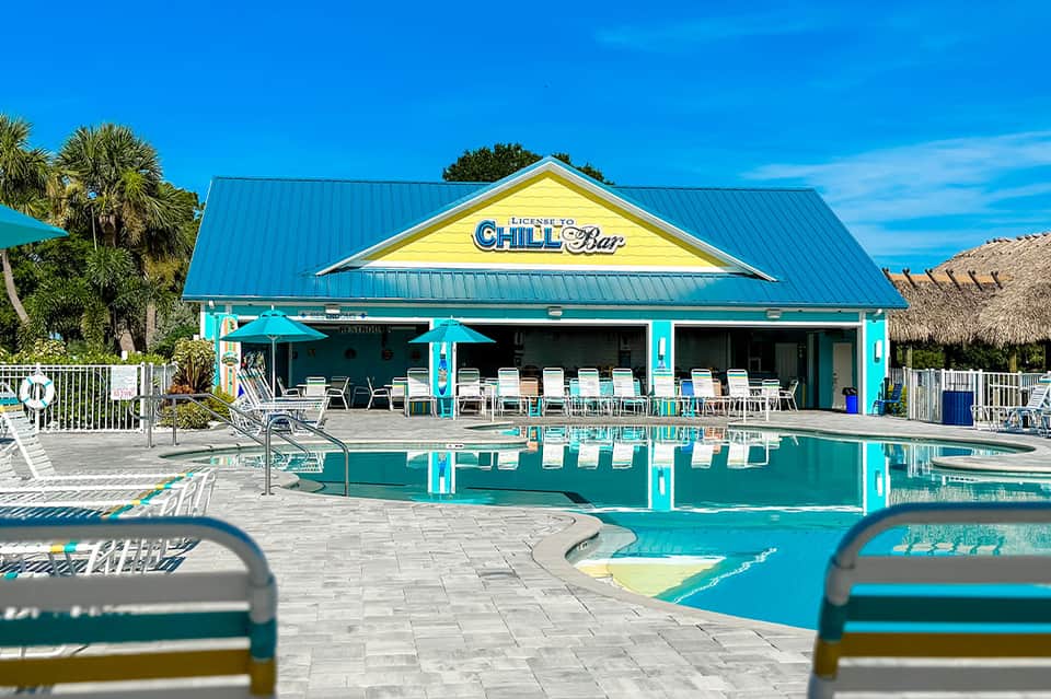 Colorful pool bar with turquoise trim, yellow gabled roof, and palm tree landscaping