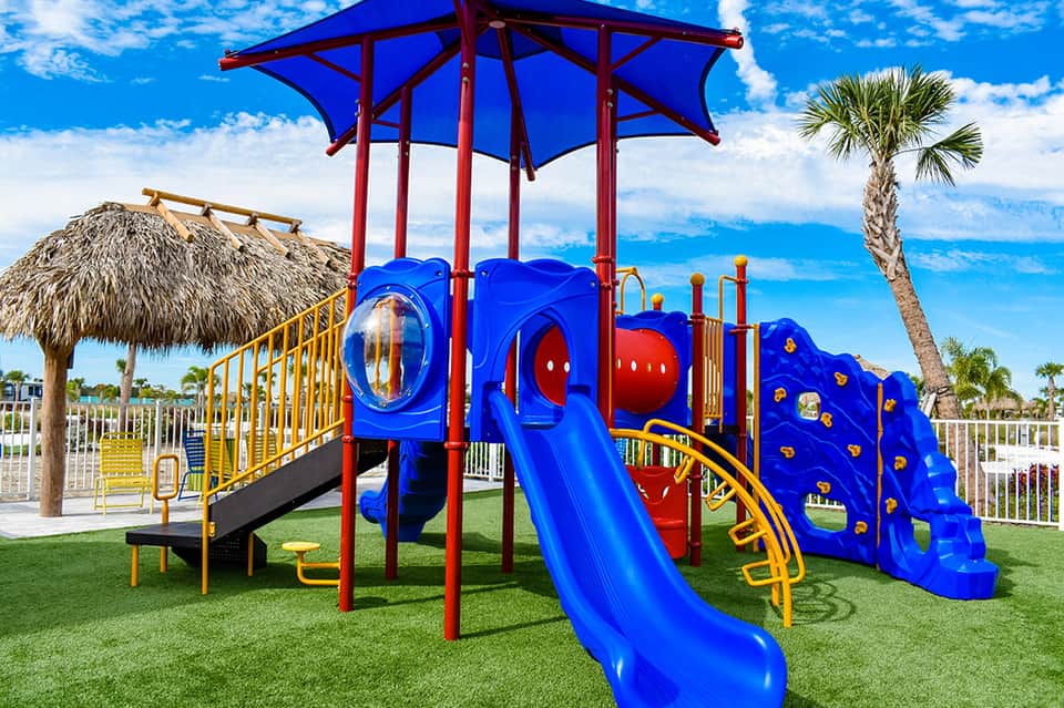 Colorful children's playground with blue slide structure and palm trees on green grass