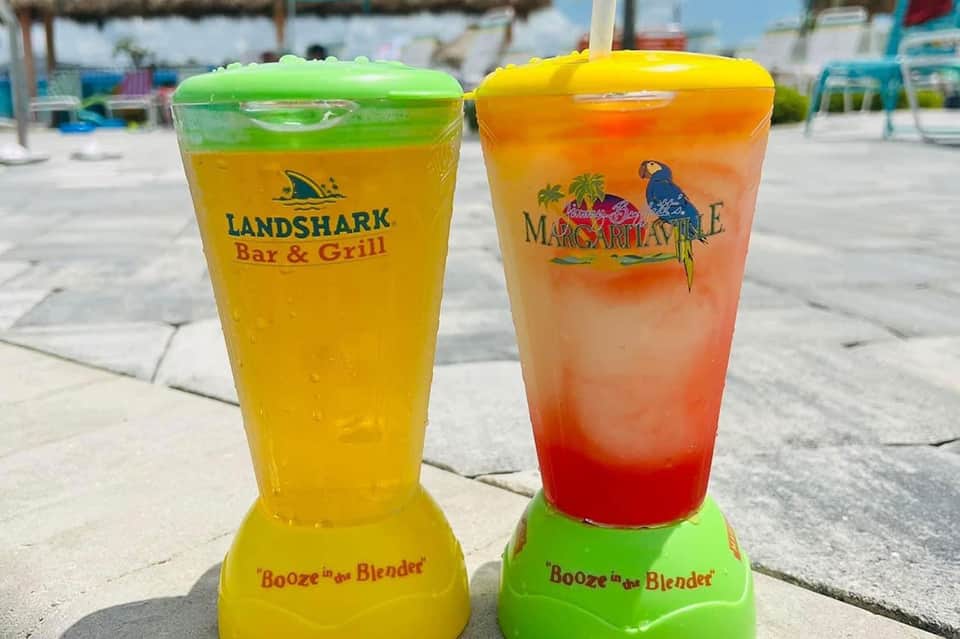 Two blended cocktails in colorful cups at poolside bar