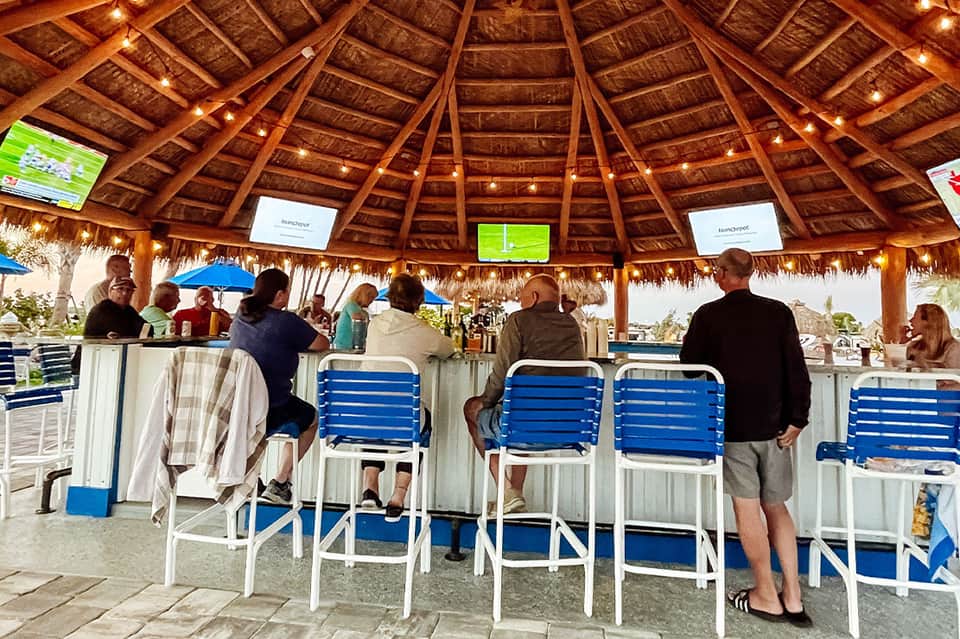 Tiki bar with thatched roof, wooden structure, blue lounge chairs, and ocean backdrop