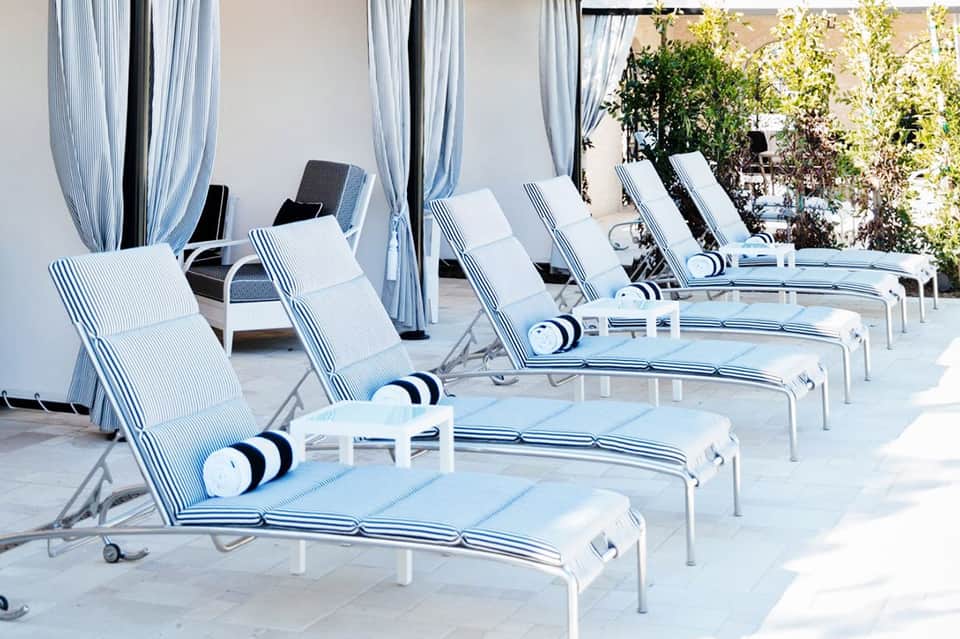 Row of striped lounge chairs with blue and white cushions on a sunny terrace with curtained cabanas