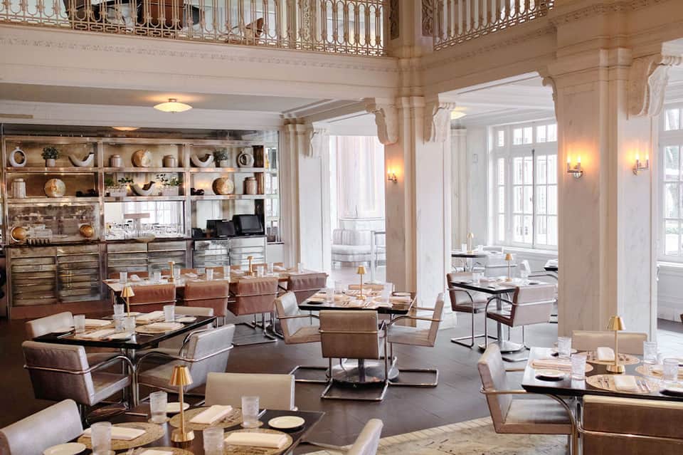 Elegant fine dining restaurant with tan leather chairs, decorative shelving, and ornate railings