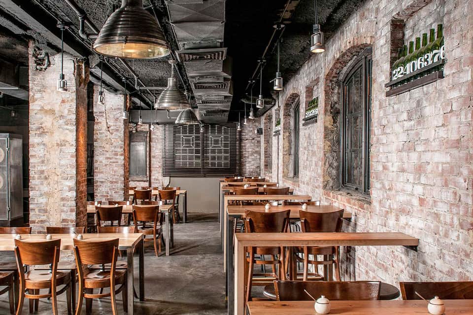 Industrial-style dining space with brick walls, wooden tables, pendant lighting, and metal structural beams