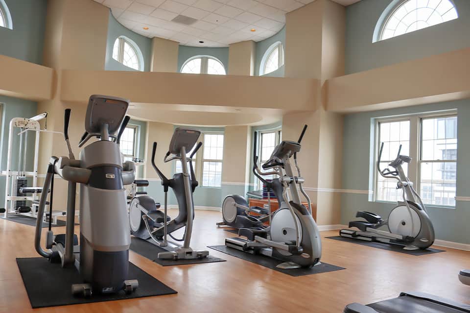 Fitness center with cardio equipment, arched windows, and natural daylight
