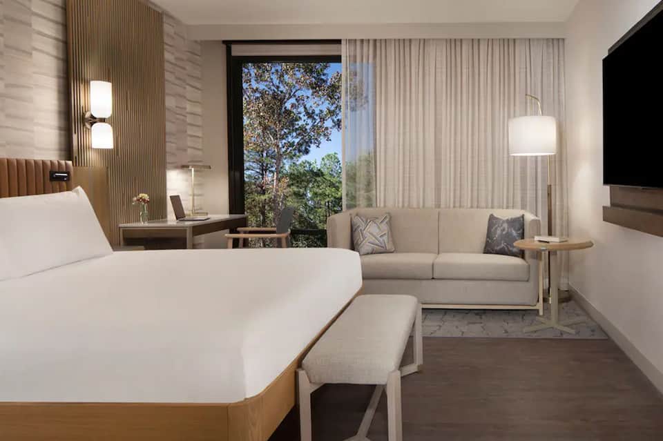 Modern hotel guest room with bed, sofa, large window, and contemporary furnishings