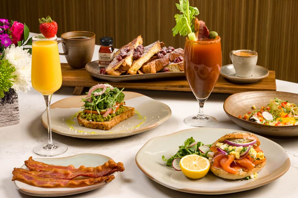 Gourmet breakfast spread with eggs, bacon, toast, fresh juice, cocktails, and plated dishes