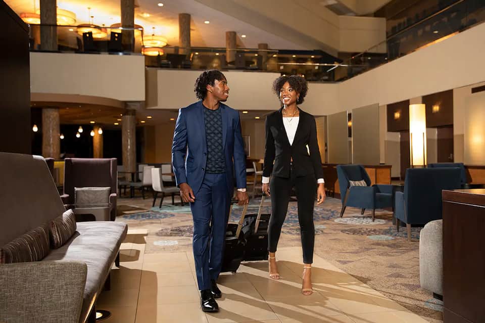 Man and woman in business attire walking through elegant hotel lobby with high ceilings