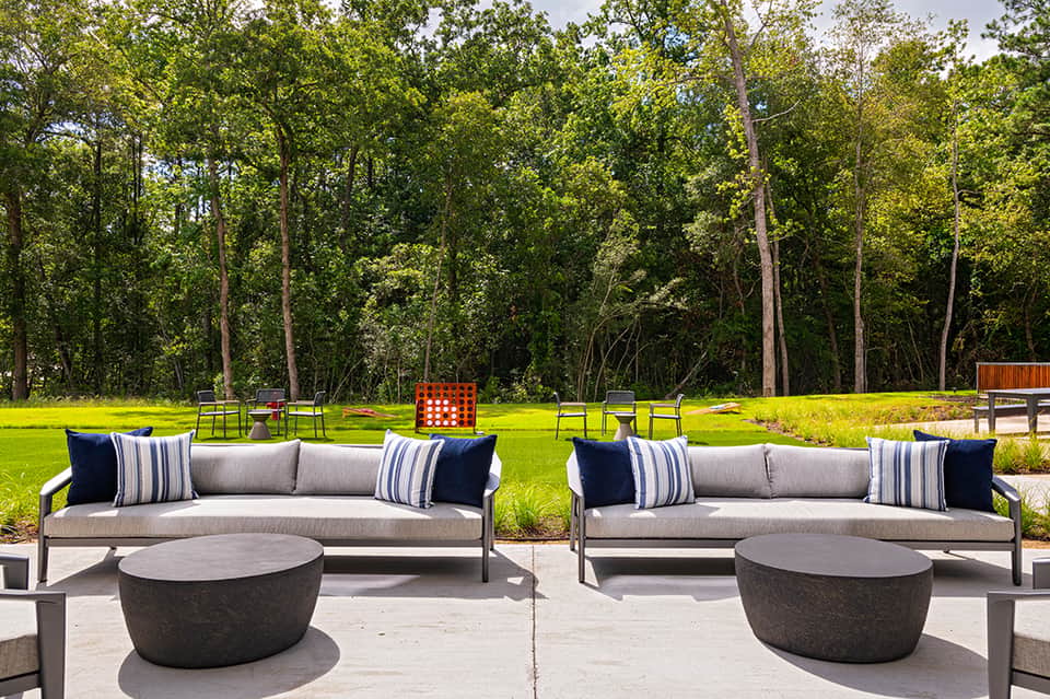 Modern outdoor seating area with gray sofas, fire table, and forest backdrop