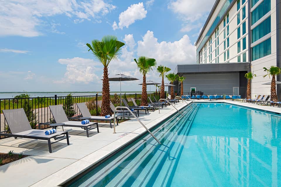 Resort rooftop pool with palm trees, lounge chairs, umbrellas, and waterfront views