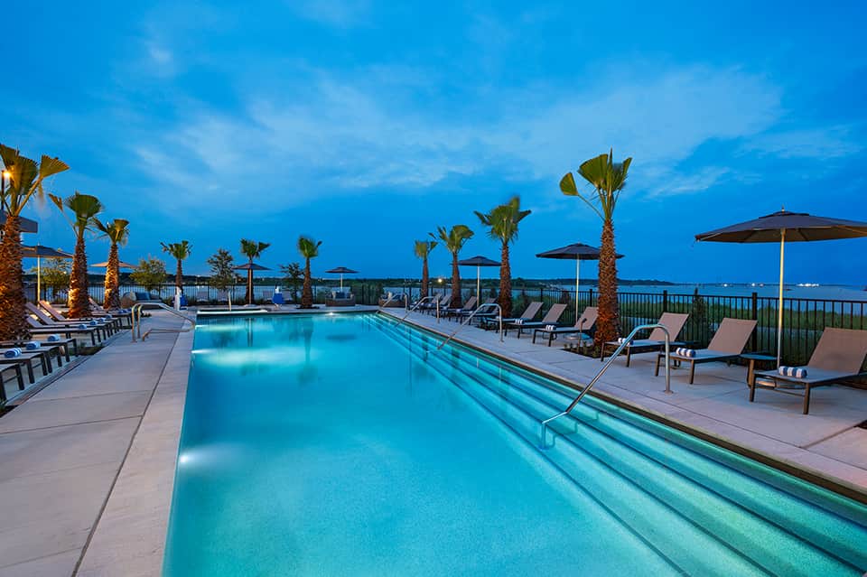 Nighttime resort lap pool with lounge chairs, palm trees, and ocean view lighting