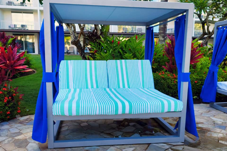 Modern blue and white cabana bed with striped cushions set on stone patio overlooking manicured lawn