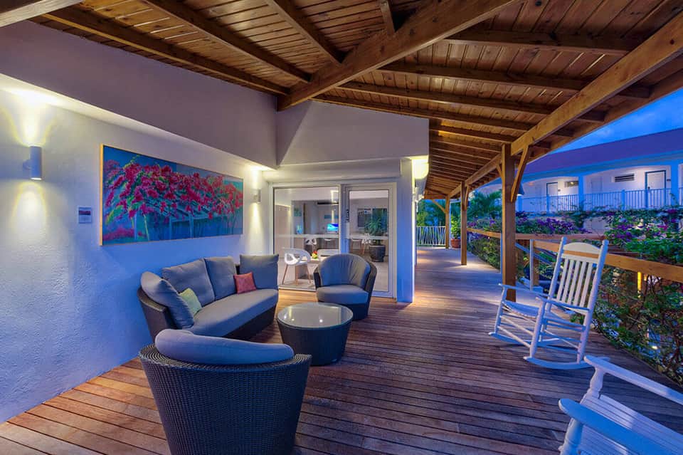 Twilight deck with wicker seating, wooden beams, blue accent wall, and ocean view