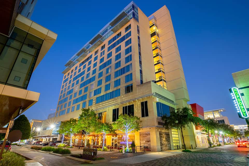 Upscale hotel building at night with illuminated storefront, yellow accent lighting, and street-level shops