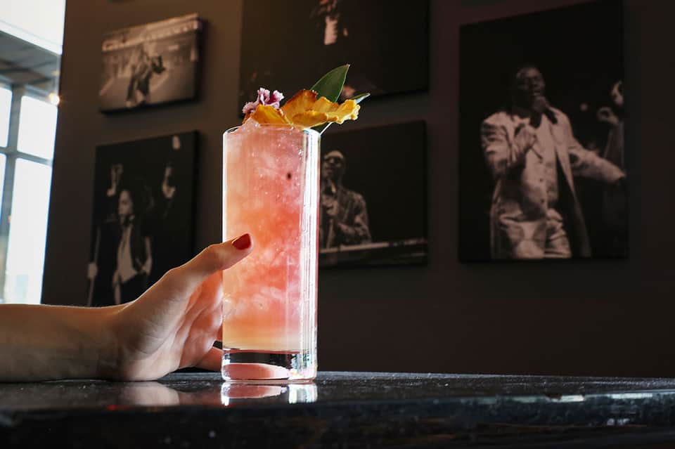 Hand holding a pink tropical cocktail with flower garnish at an upscale resort bar