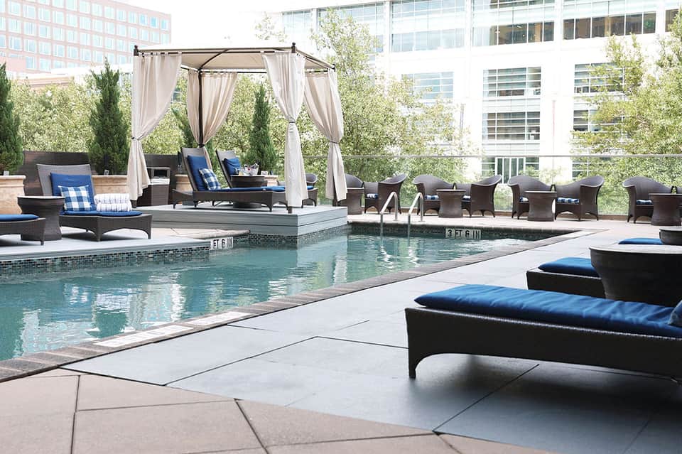 Urban rooftop pool with white cabana, lounge chairs, and city buildings