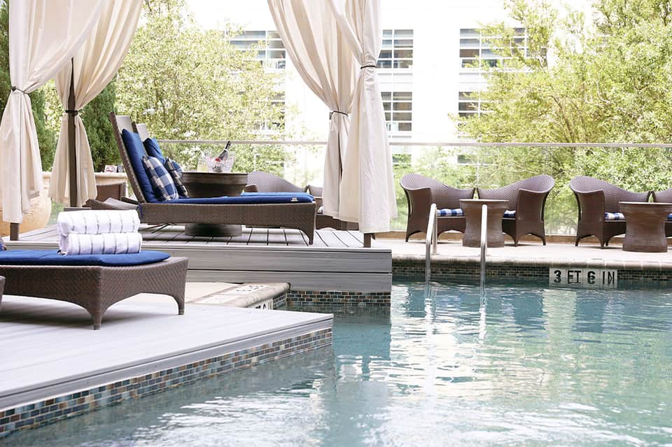 Luxury pool area with lounge chairs, draped cabanas, wicker seating, and city views