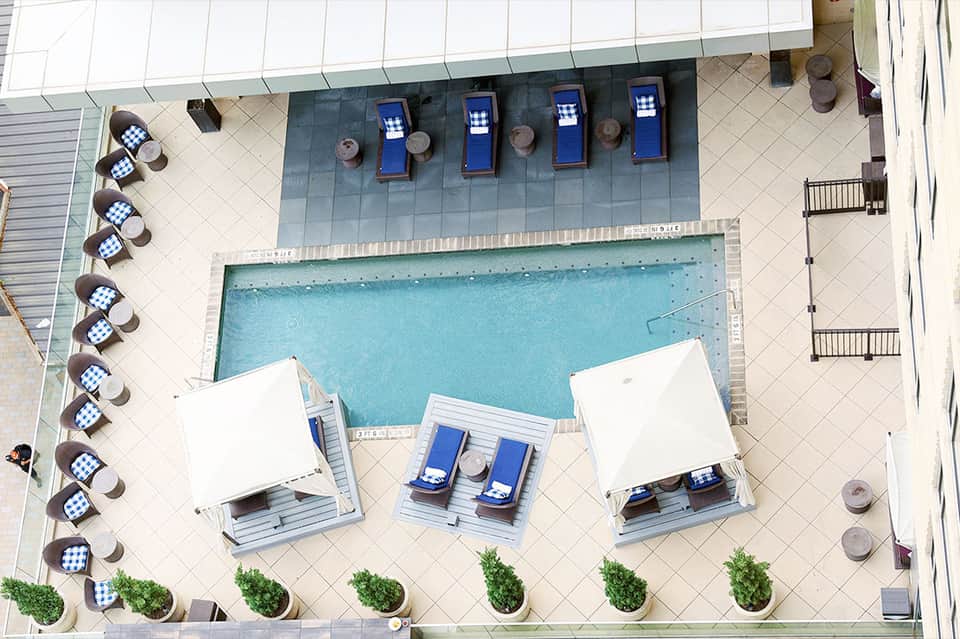 Overhead view of resort pool with white umbrellas, blue loungers, and organized deck seating area