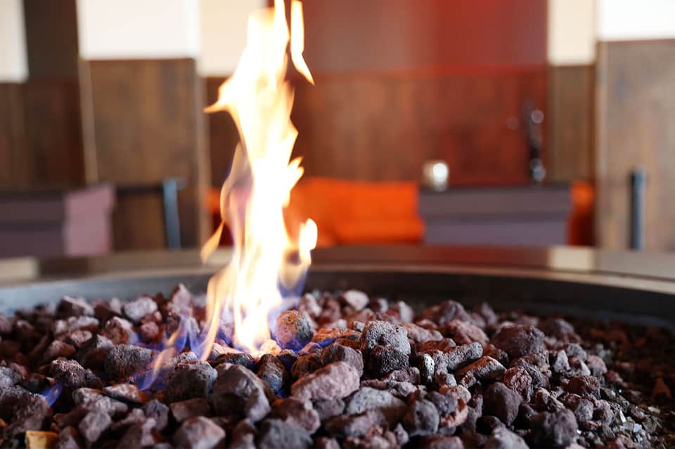 Fireplace with flames and decorative rocks in modern lounge with blurred seating in background