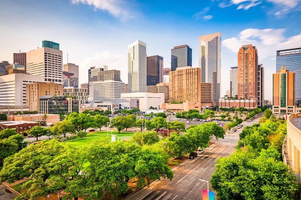 Downtown city skyline with tall buildings, green parks, and urban landscape under blue sky